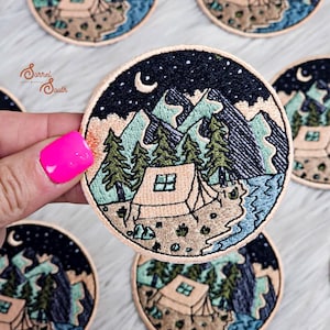 Può includere: Toppa rotonda ricamata raffigurante una scena di campeggio con una tenda, montagne, alberi e una luna crescente sotto un cielo stellato. La toppa ha un bordo beige. Il testo "Sorrel South" è visibile.