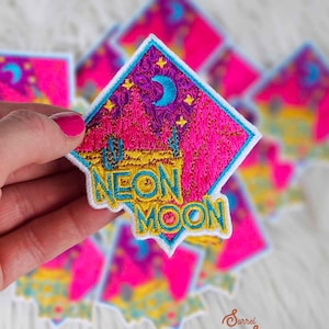 May include: Embroidered patch with a neon pink and purple night sky design, featuring a crescent moon and stars. The patch has a turquoise border and the words "NEON MOON" in yellow. Several patches are visible.