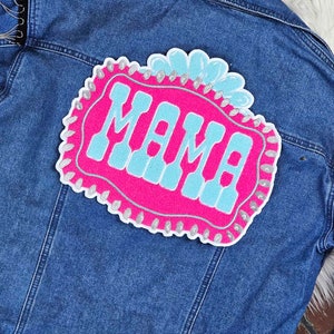 May include: A denim jacket with a pink and blue embroidered patch that says "MAMA" with silver glitter accents.