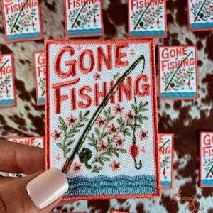 May include: Embroidered patch with the words "GONE FISHING" in red, featuring a fishing rod, flowers, and a red bobber. The patch is white with a red border and a blue water design.
