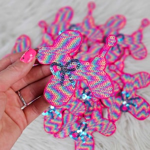 May include: A pile of colorful, sequined iron-on patches shaped like a balloon dog. The patches have a rainbow chevron pattern and a blue bow.