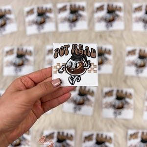 May include: White square patch with the words "POT HEAD" in brown letters. The patch features a cartoon coffee pot character with a peace sign. Many similar patches are in the background.