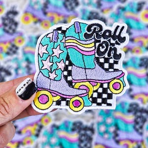 Op de afbeelding: Een kleurrijk geborduurd patch met een paar rol schaatsen op een geruite achtergrond en de tekst "Roll On".
