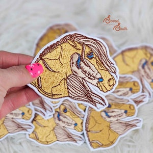 May include: A stack of embroidered iron-on patches featuring a horse's head with a brown mane and blue eyes. The patches are white with a yellow background and are perfect for adding a touch of equestrian style to clothing, bags, or other accessories.