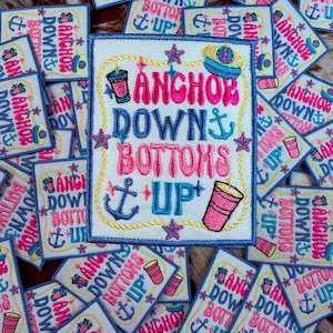 Può includere: Toppe ricamate con la frase "Anchor Down, Bottoms Up" in rosa e blu. Le toppe presentano ancore, stelle e un disegno di tazza rosa. Le toppe sono su sfondo bianco con un bordo blu.