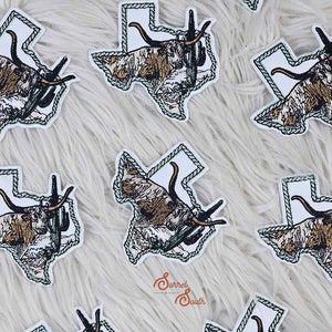 Puede incluir: Varios parches bordados para planchar en forma del estado de Texas, con un toro longhorn y un cactus. Los parches están rodeados por un diseño de cuerda y tienen un fondo blanco.