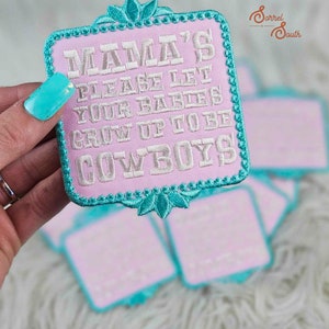 May include: A pink and turquoise embroidered patch with the text "Mama's Please Let Your Babies Grow Up To Be Cowboys".