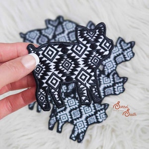Puede incluir: Un conjunto de cinco parches bordados de hierro en blanco y negro con forma de cerdo con un patrón geométrico. Los parches están sobre una superficie blanca y peluda.