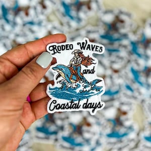May include: Embroidered patch with a white background featuring a woman riding a dolphin in blue water with the text "Rodeo Waves and Coastal Days".