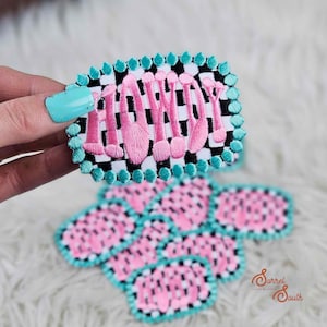 Puede incluir: Parches bordados con temática de maquillaje. Los parches presentan brochas de maquillaje rosas sobre un fondo a cuadros blanco y negro, enmarcados por un borde turquesa. También se ven parches adicionales con un diseño de lunares rosas y negros.