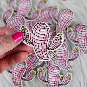 Puede incluir: Un montón de parches de cactus de vichy rosa y blanco con costuras marrones. Los parches están bordados con flores amarillas.