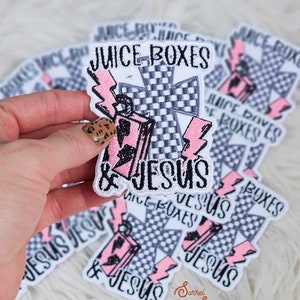 以下が含まれることがあります： 白地に黒と白の市松模様の十字架、ピンクのジュースボックス、そして「ジュースボックス＆ジーザス」という文字が書かれたアイロン接着パッチです。