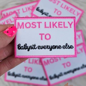 May include: White rectangular patch with pink embroidered border and text. The text reads "MOST LIKELY TO" in pink, with "babysit everyone else" in black script. Several similar patches are in the background.