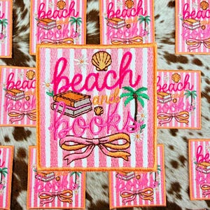 May include: Pink and white striped embroidered patches with the words "beach and books" in cursive. The patches feature a seashell, palm tree, and a stack of books. The patches have an orange border and a bow.