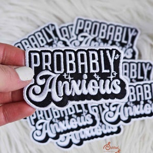 Op de afbeelding: Close-up van verschillende zwarte en witte geborduurde strijklabels met de tekst "Probably Anxious" in een wit cursief lettertype.