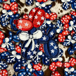 May include: A collection of red, white, and blue balloon dog patches. The patches feature a patriotic design with stars and bows. The background has a brown and white cowhide pattern.