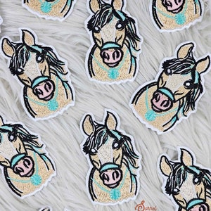 May include: Multiple embroidered patches of a horse's head with a turquoise necklace. The horse has a light brown coat, black mane, and pink nose.