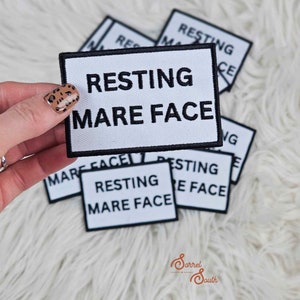May include: A white patch with black text that reads "RESTING MARE FACE". The patch is surrounded by other similar patches with the same text.