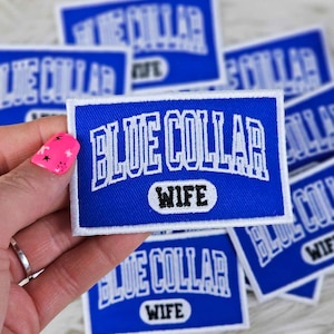 Può includere: Toppa ricamata blu e bianca con il testo "Blue Collar Wife" in un ovale bianco. La toppa è su una superficie bianca e pelosa.