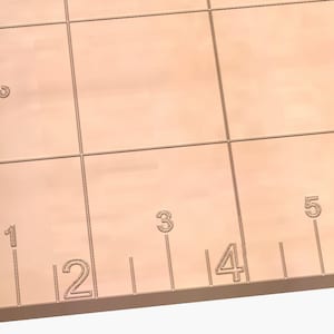 May include: A close-up of a light brown cutting mat with a grid pattern and inch measurements along the bottom edge. The numbers 0, 1, 2, 3, 4, 5, 6, 7, and 8 are visible.