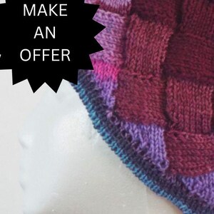 May include: A knitted hat with a patchwork design in shades of purple, pink, blue, and burgundy.