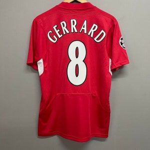 Peut inclure: Un maillot de sport rouge à manches courtes avec le nom GERRARD et le numéro 8 imprimés en blanc avec des contours noirs au dos. Le maillot présente des panneaux latéraux blancs et un emblème circulaire sur la manche droite avec un motif étoilé.