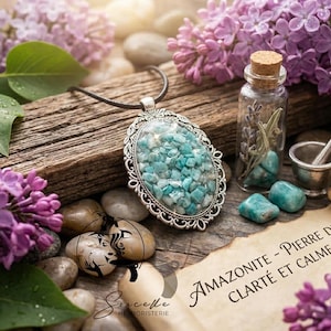 May include: An oval pendant with a silver filigree frame, filled with small, light blue stones, hangs on a black cord. The image includes a small glass bottle, a mortar and pestle, and a scroll, all surrounded by purple flowers.