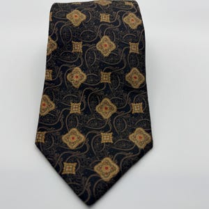 May include: A necktie featuring a dark navy blue background with a repeating pattern of gold and red quatrefoil shapes interspersed with smaller square motifs and thin, swirling, light-colored vine-like lines across the entire fabric surface.