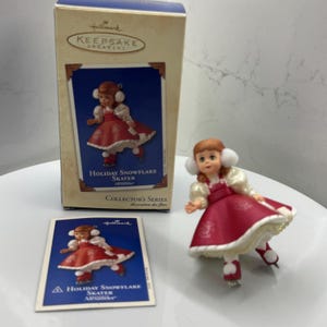 Può includere: Un ornamento Hallmark Keepsake di una pattinatrice. La statuina indossa un vestito rosso con finiture bianche e paraorecchie. La scatola e la carta presentano anche la stessa immagine e il testo: "Holiday Snowflake Skater".