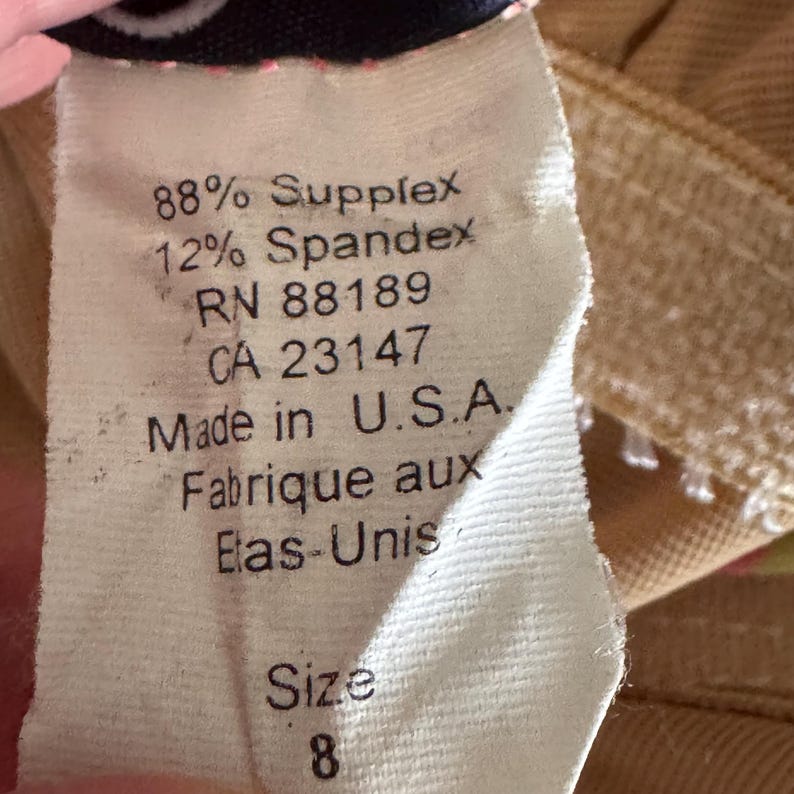 K&ouml;nnte beinhalten: Nahaufnahme eines Kleidungsetiketts mit dem Text: "88% Supplex, 12% Spandex, RN 88189, CA 23147, Made in U.S.A., Fabrique aux Elas-Unis, Gr&ouml;&szlig;e 8."