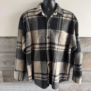 May include: A button-down, plaid shirt in black, tan, and gray. The shirt has a collared neckline, long sleeves, and a soft, textured appearance. The plaid pattern is a classic design, suitable for casual wear.