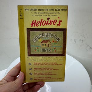 May include: A vintage paperback book titled "Heloise's Housekeeping Hints." The cover features a framed image of a house and the title in red. The book is yellow with text that reads "Over 350,000 copies sold."