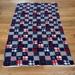 May include: A rectangular fabric piece featuring a patchwork design of alternating squares in navy blue, white, and red. The pattern includes various motifs such as small floral prints, gingham checks, and plaid designs arranged in a grid layout.