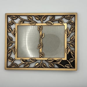 Può includere: Una cornice rettangolare dorata con un design a foglie. La cornice ha due aperture per le foto e un bordo decorativo di foglie e viti. La cornice è in metallo e ha un aspetto vintage.