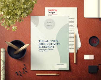 May include: An overhead shot of a workspace featuring a planner titled "The Aligned Productivity Blueprint." The image includes pencils, a small bowl, push pins, and a notepad. The color scheme is neutral with pops of red.