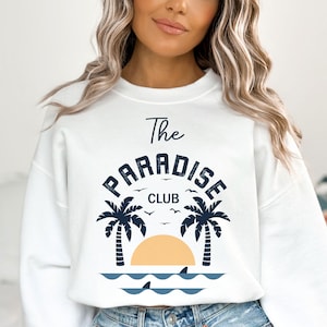 May include: White sweatshirt with a blue graphic print of palm trees, a sunset, and the text "The Paradise Club".