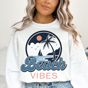 May include: White sweatshirt with a blue and pink graphic of a palm tree, sailboat, and the words "Beach Vibes".