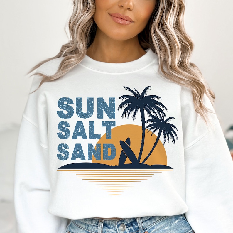 May include: White sweatshirt with a graphic design of palm trees, a sunset, and the text "SUN SALT SAND" in a distressed blue font.