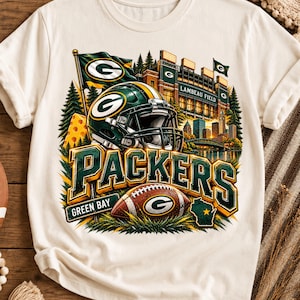 May include: A cream-coloured t-shirt featuring a graphic of a Green Bay Packers football helmet, a football, Lambeau Field, and the text "PACKERS" and "GREEN BAY". The design includes a cheese wedge, pine trees, and a map of Wisconsin.