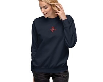 May include: Navy blue sweatshirt with a red rose graphic and the word "ROSELY" printed below it. The sweatshirt is a long-sleeved, crew neck style. The model is wearing black jeans.