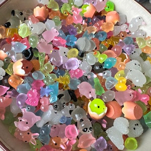 May include: A large collection of colorful, translucent, and opaque plastic figurines. The figurines are shaped like animals, flowers, and other objects. They are arranged in a bowl.