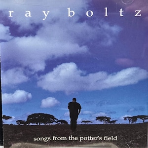 May include: A CD case featuring the album "Songs from the Potter's Field" by Ray Boltz. The cover art depicts a person walking towards the horizon under a cloudy blue sky. The artist's name is in white letters at the top.