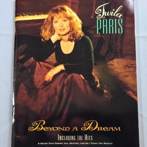 May include: Album cover for Twila Paris's "Beyond a Dream." The cover features a woman with auburn hair in a dark green top and burgundy skirt. The album title and artist name are in elegant script. Includes the hits "A Heart That Knows You, Destiny, and Do I Trust You Medley."