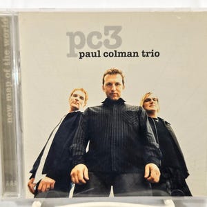 May include: A CD case featuring the album "pc3" by the Paul Colman Trio. The cover has a light background with the band's name and three men in dark clothing. The spine reads "new map of the world."
