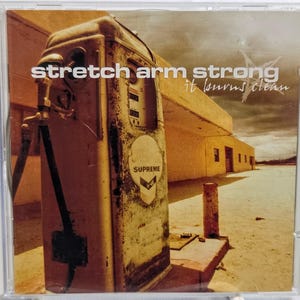 May include: CD case featuring the album "it burns clean" by Stretch Arm Strong. The cover art depicts a weathered gas pump with the word "Supreme" and a chevron logo. The background shows a desert landscape.