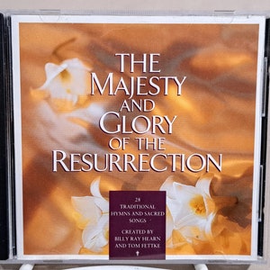 May include: A CD case with a white background and a floral design. The text on the case reads "The Majesty and Glory of the Resurrection" and "28 Traditional Hymns and Sacred Songs. Created by Billy Ray Hearn and Tom Fettke."