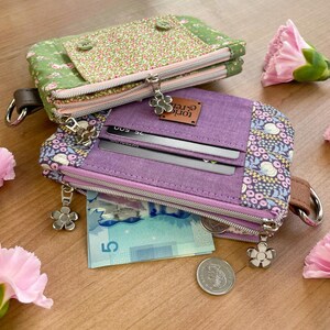 May include: Two fabric wallets with floral and solid patterns. One is green with pink flowers, the other is purple with a floral pattern and a leather tag that says "tori & ren". Both have zippers and flower-shaped zipper pulls.