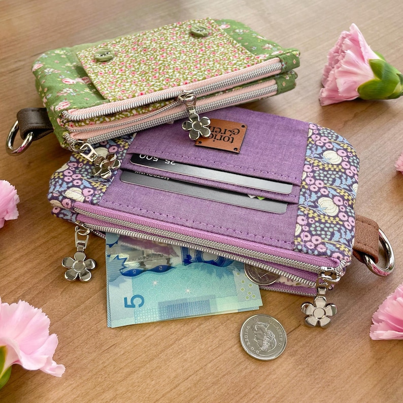 May include: Two fabric wallets with floral and solid patterns. One is green with pink flowers, the other is purple with a floral pattern and a leather tag that says "tori & ren". Both have zippers and flower-shaped zipper pulls.