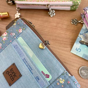 May include: A blue floral print wallet with a brown zipper and a heart-shaped zipper pull. The wallet has a small brown leather tag that reads "tori & ren". Inside the wallet are two cards and a driver's license.