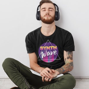 Puede incluir: Una camiseta negra con un diseño gráfico de un círculo morado con el texto "SYNTH Wave" en una fuente de estilo retro. El círculo está dentro de un triángulo blanco.
